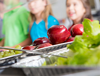 Closeup of apples and lettuce; children in lunch line