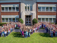 Students and teacher form an "M" shape in front of the Midway school building 