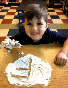 K student write letter F in cream with big smile